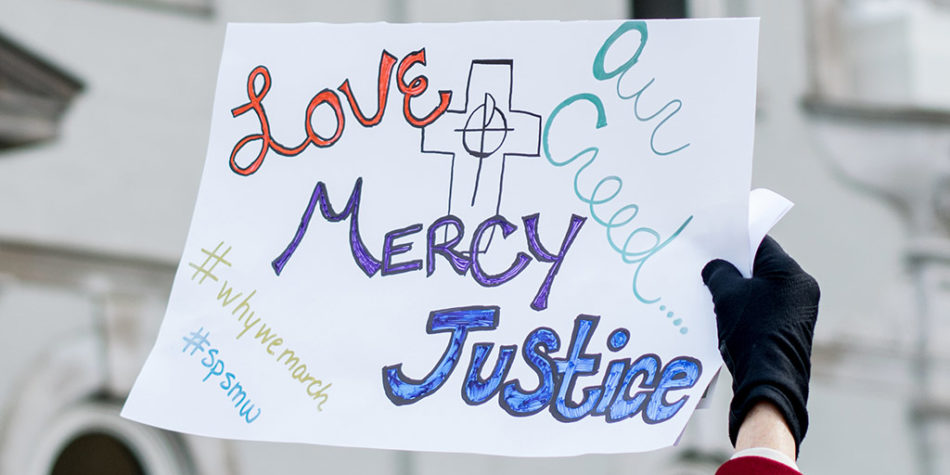 hand holding a sign saying "love mercy justice"