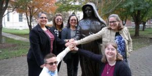 A group of young Sisters of Providence smile with the bronze statue of Mother Theodore