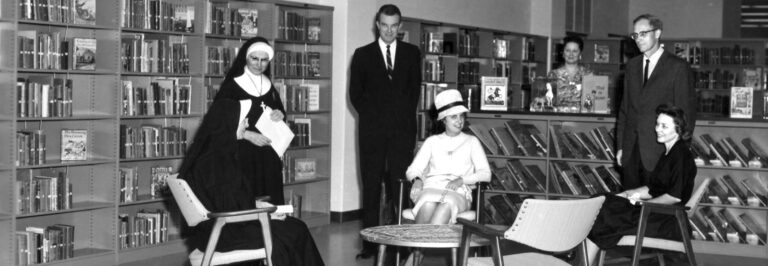 Women and men smile with a sister in a library
