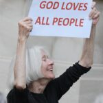 A smiling sister holding a sign that says "God loves all people"
