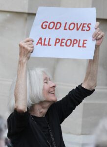A smiling sister holding a sign that says "God loves all people"