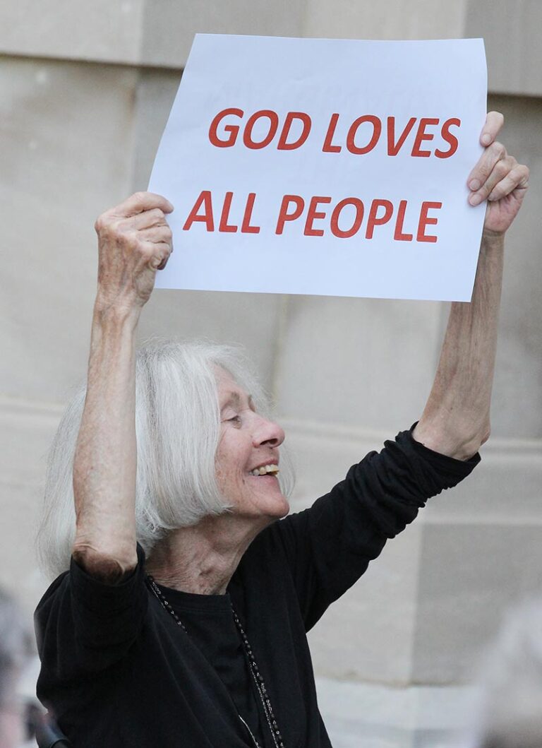 A smiling sister holding a sign that says "God loves all people"