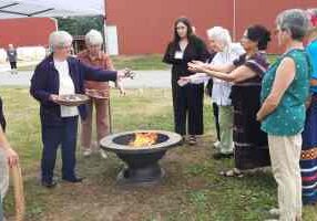 Sister Jan Craven and Sister Marsha Speth (left) toss tobacco bags into the sacred fire during the blessing of the green space.