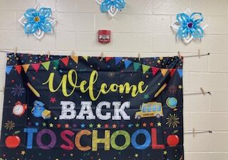 This photo is our colorful welcome back to school sign, which shows the excitement. Above the welcome sign are handmade decorations featuring flowers. 